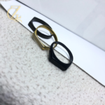 Close-up of a men's rectangular stainless steel ring featuring a black enamel Greek Key meander pattern on a polished gold and silver band.