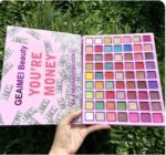 A large makeup kit displaying 63 square pans of highly pigmented eyeshadows, showcasing vibrant shades of blues, teals, greens, and purples in matte, shimmer, and glitter finishes.