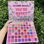 A large makeup kit displaying 63 square pans of highly pigmented eyeshadows, showcasing vibrant shades of blues, teals, greens, and purples in matte, shimmer, and glitter finishes.